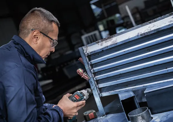 Una persona que usa equipo de seguridad perfora un marco de ventilación de metal.