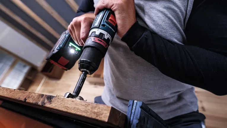 Persona que utiliza un taladro inalámbrico sobre una tabla de madera en un taller.