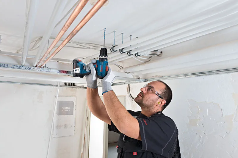 Una persona que usa equipo de seguridad perfora un techo para instalar un conducto eléctrico.