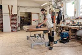 Una persona que usa equipo de seguridad lija una superficie de madera con una lijadora orbital aleatoria inalámbrica.