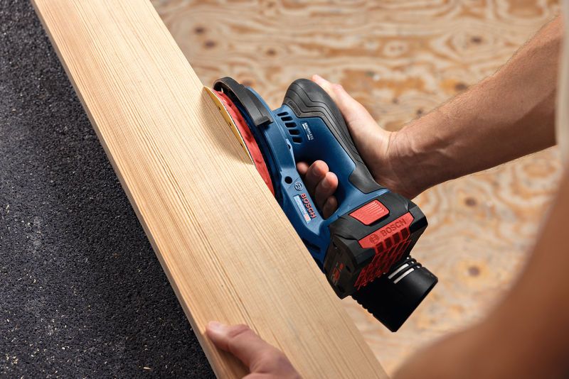 Persona lijando una tabla de madera utilizando una lijadora orbital aleatoria inalámbrica.