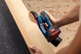 Persona lijando una tabla de madera utilizando una lijadora orbital aleatoria inalámbrica.