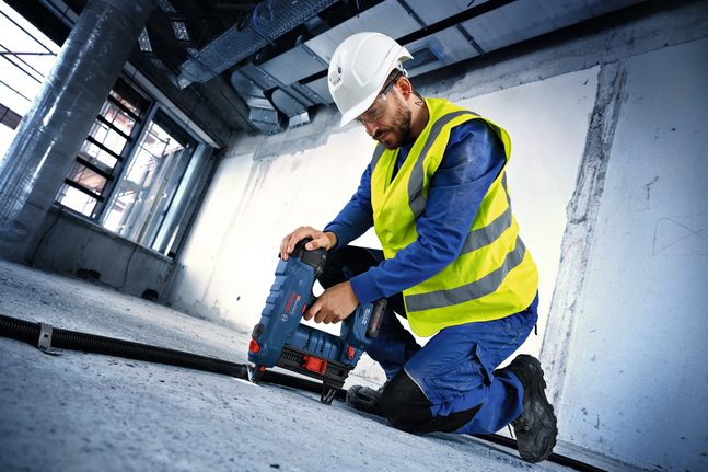 Una persona que usa equipo de seguridad utiliza una herramienta eléctrica para perforar un piso de concreto.