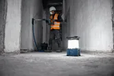 Un trabajador que usa equipo de seguridad perfora una pared con una luz de trabajo inalámbrica en el piso.