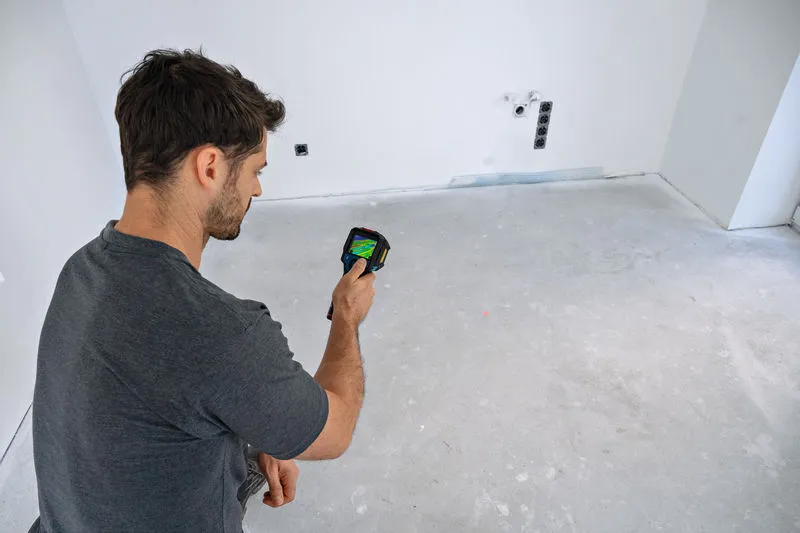 Una persona examina el suelo vacío de una habitación con una cámara térmica.