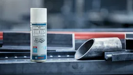 Lata de aerosol de aceite de corte colocada en un banco de trabajo de metal al lado de tubos de acero.