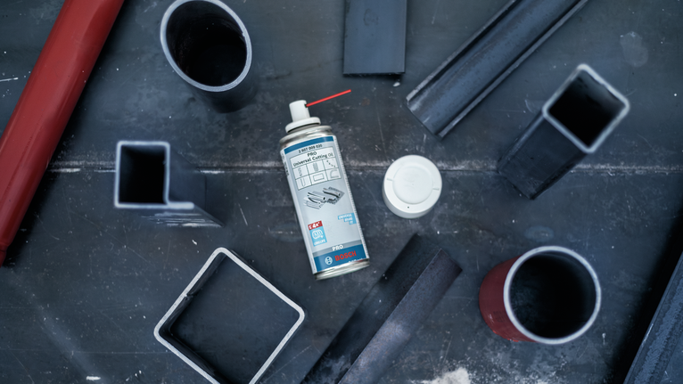 Lata de aerosol colocada sobre un banco de trabajo de metal rodeado de varios tubos de acero.