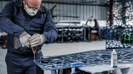 Una persona que usa equipo de seguridad perfora metal con una herramienta eléctrica en un taller.