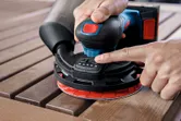 Una persona utiliza una lijadora orbital aleatoria inalámbrica para alisar tablones de madera.