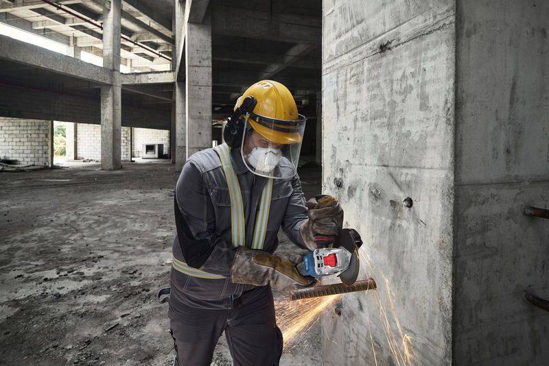 Una persona que usa equipo de seguridad pule una pared de hormigón con una amoladora angular, produciendo chispas.