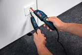Una persona prueba una toma de corriente eléctrica con un comprobador de voltaje sobre un piso alfombrado.
