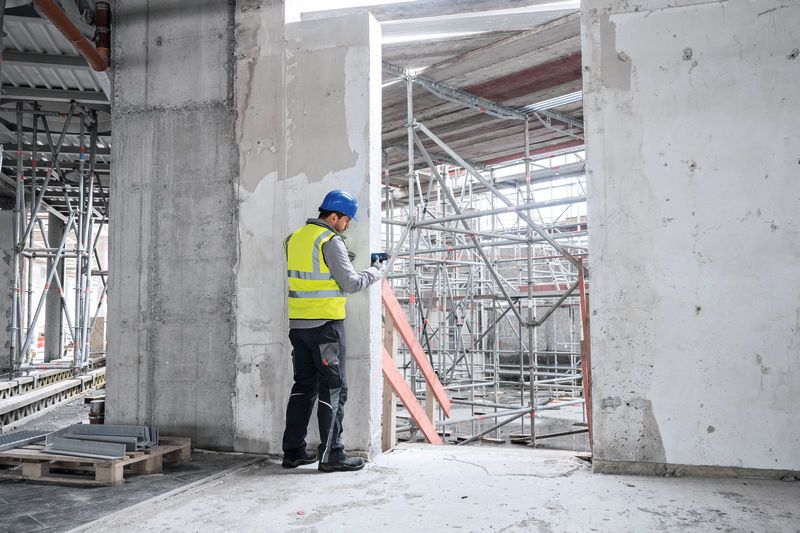 Una persona que lleva equipo de seguridad utiliza un medidor láser en una obra en construcción.