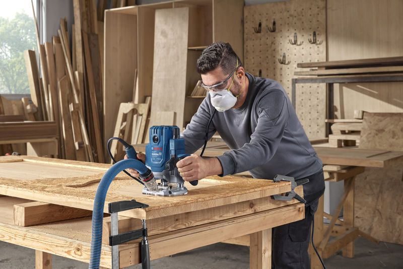 Una persona que usa equipo de seguridad utiliza una fresadora para dar forma a la madera en un taller.