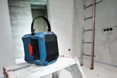 Radio portátil para obra con asa de transporte colocada sobre una escalera de mano en una habitación en construcción.