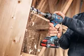 Una persona utiliza un taladro inalámbrico para hacer un agujero en una tabla de madera.