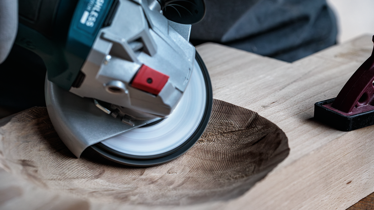 Una persona utiliza una amoladora angular para tallar una forma suave y cóncava en una tabla de madera.