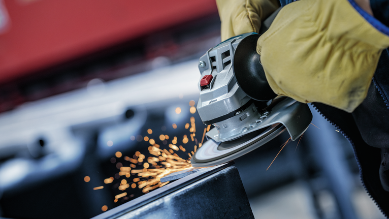 Persona que usa equipo de seguridad muele metal, produciendo chispas.