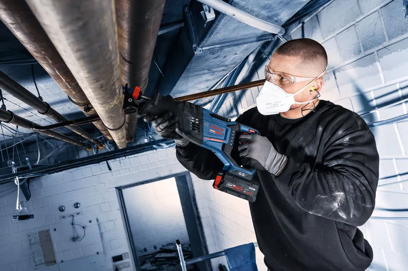 Una persona que usa equipo de seguridad utiliza una sierra alternativa inalámbrica para cortar tuberías elevadas.