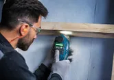 Una persona que usa equipo de seguridad corta madera con una cortadora múltiple inalámbrica.