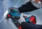 Una persona que usa equipo de seguridad utiliza un multicortador inalámbrico sobre una superficie metálica.