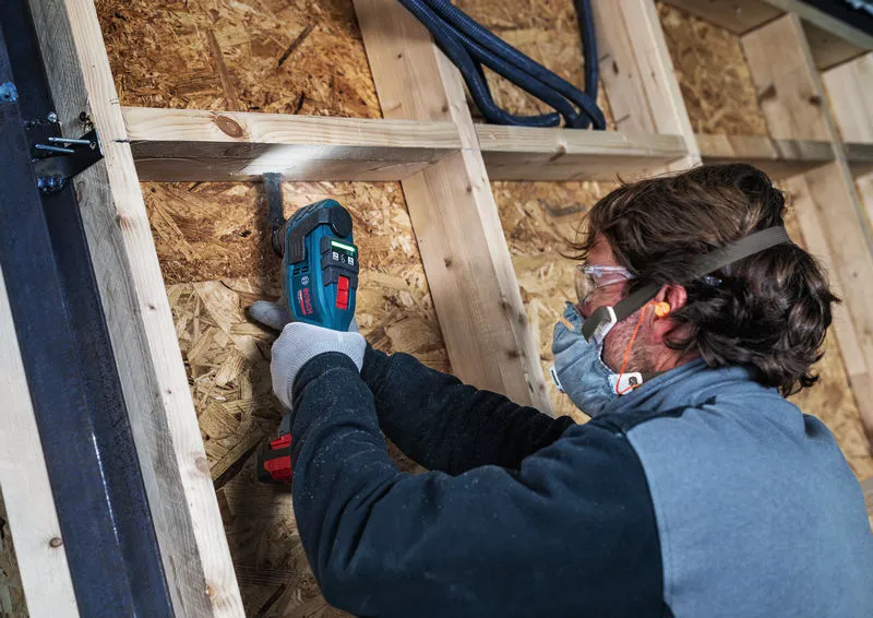 Una persona que usa equipo de seguridad utiliza un cortador múltiple inalámbrico para trabajar en estructuras de madera.