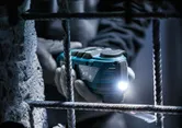 Una persona que usa equipo de seguridad utiliza un multicortador inalámbrico con una luz LED cerca de una barra de refuerzo.
