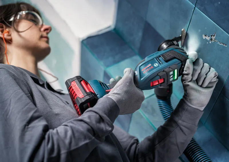 Una persona que usa equipo de seguridad utiliza un cortador múltiple inalámbrico para cortar baldosas.