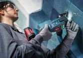Una persona que usa equipo de seguridad utiliza un cortador múltiple inalámbrico para cortar baldosas.