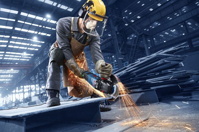 Una persona que usa equipo de seguridad utiliza una amoladora angular para cortar metal, lo que produce chispas.