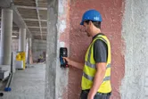 Una persona que lleva equipo de seguridad examina una pared de hormigón con un detector.