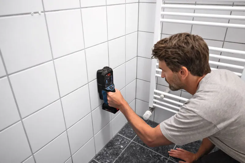 Una persona escanea la pared de azulejos del baño con un dispositivo detector.