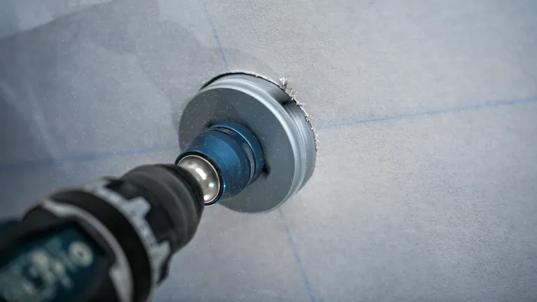 Un taladro eléctrico con un accesorio de sierra de corona corta un agujero circular en una pared.