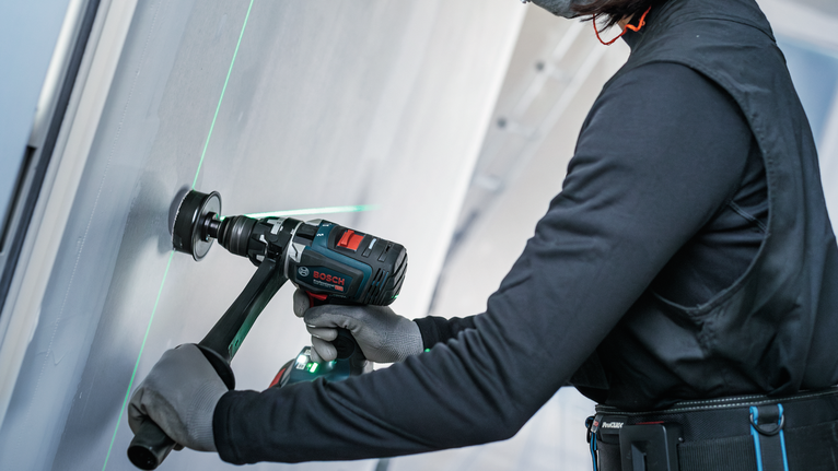 Una persona que usa equipo de seguridad perfora una pared usando una herramienta eléctrica.