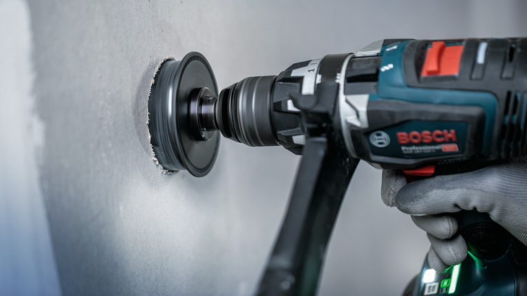 Una persona que usa equipo de seguridad perfora un agujero en una pared con una herramienta eléctrica.