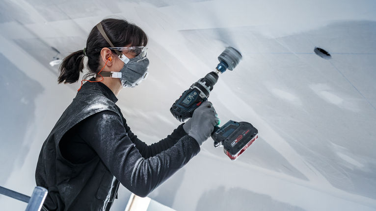 Una persona que usa equipo de seguridad perfora un techo con una herramienta eléctrica inalámbrica.