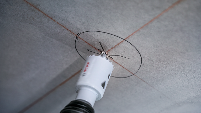 Una sierra de corona perfora una abertura circular en un panel de techo marcado.
