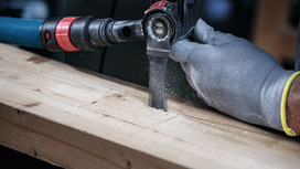 Una persona que usa equipo de seguridad corta una tabla de madera con una sierra alternativa.
