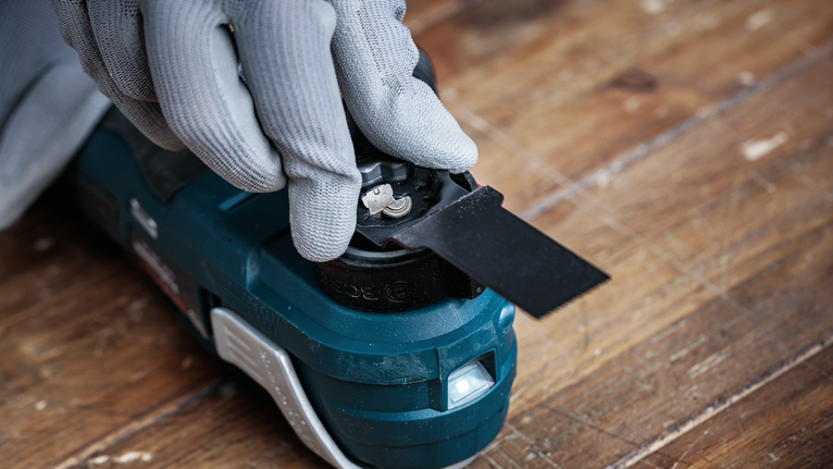 Una persona que usa equipo de seguridad fija una cuchilla a una herramienta eléctrica sobre una superficie de madera.