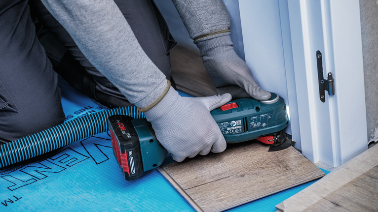 Una persona que usa equipo de seguridad utiliza una herramienta inalámbrica para cortar pisos laminados.