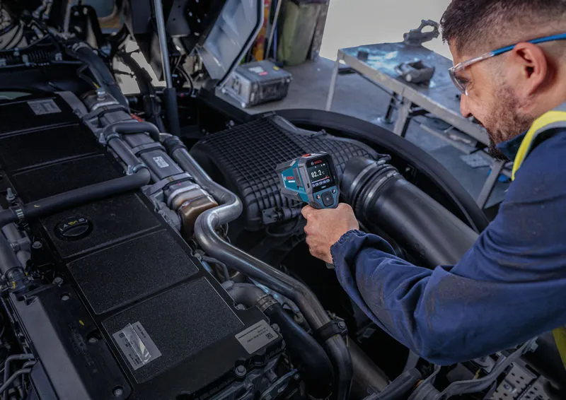 Una persona que lleva puesto el equipo de seguridad utiliza un detector térmico para comprobar la temperatura del motor.