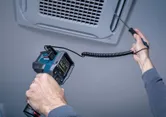 Una persona utiliza un termómetro para medir la temperatura en una rejilla de ventilación.