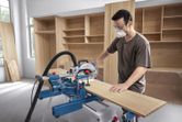 Una persona que usa equipo de seguridad utiliza una sierra ingletadora para cortar una tabla de madera.