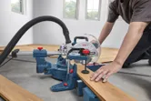 Una persona que usa equipo de seguridad corta una tabla de madera con una sierra ingletadora.