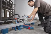 Una persona que usa equipo de seguridad corta una viga de metal usando una sierra ingletadora.