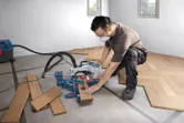 Una persona que usa equipo de seguridad utiliza una sierra ingletadora para cortar paneles de piso de madera.