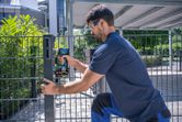 Una persona que usa equipo de seguridad utiliza una llave de impacto inalámbrica para fijar un poste de cerca de metal.