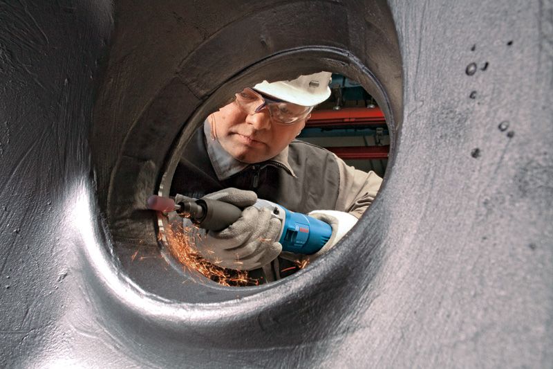 Una persona que usa equipo de seguridad muele metal dentro de un tubo grande, creando chispas.