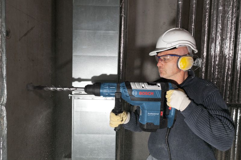 Una persona que usa equipo de seguridad perfora una pared de hormigón utilizando un martillo perforador.