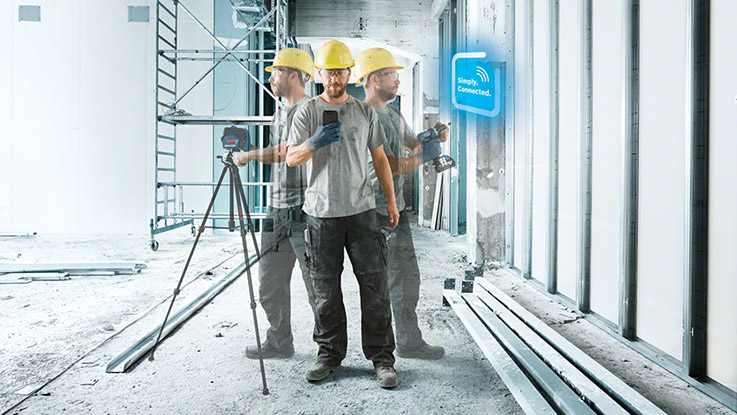 Hombre con casco amarillo usa herramientas en obra con estructuras metálicas y paredes de yeso.