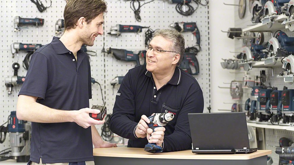 Dos hombres conversan en una tienda, uno sostiene una herramienta y el otro un medidor.